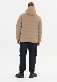 Beige puffjacka med huva, med horisontella quiltade partier. Matchas med svarta cargobyxor och sportiga svarta skor.