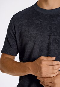 Granatowa, krótkosleeve'owa, teksturowana koszulka z okrągłym dekoltem, wyróżniająca się miękkim materiałem i subtelnością wzoru, trzymana przez rękę na tkaninie.