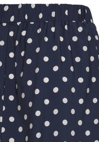 Tissu bleu marine avec une ceinture élastique, des plis froncés et un motif à pois blancs sur l'ensemble du tissu.