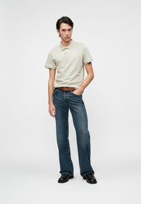 Beige polo póló, kék trapéznadrág, barna öv, fekete cipő; sima anyag, testre szabott fazon és klasszikus dizájn.