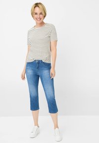 T-shirt a righe, a maniche corte, in crema e nero, abbinata a jeans blu corti e sneakers bianche. Look casual e comodo.