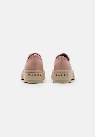 Rosa lädersneakers med en beige plattformssula, försedda med en röd logotyp på hälen och en rundad bakdel för ökat stöd.