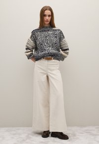 Strickpullover in Marineblau und Creme mit strukturierten Mustern, kombiniert mit cremefarbenen Weitbein-Hosen und braunen Schnürstiefeln. Mit Gürtel in der Taille.