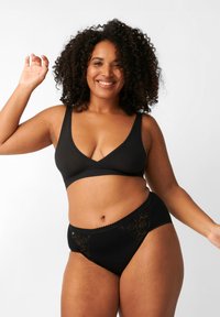 Bralette nera con scollatura a V e spalline larghe, abbinata a slip neri con dettagli in pizzo sui lati. Texture liscia.
