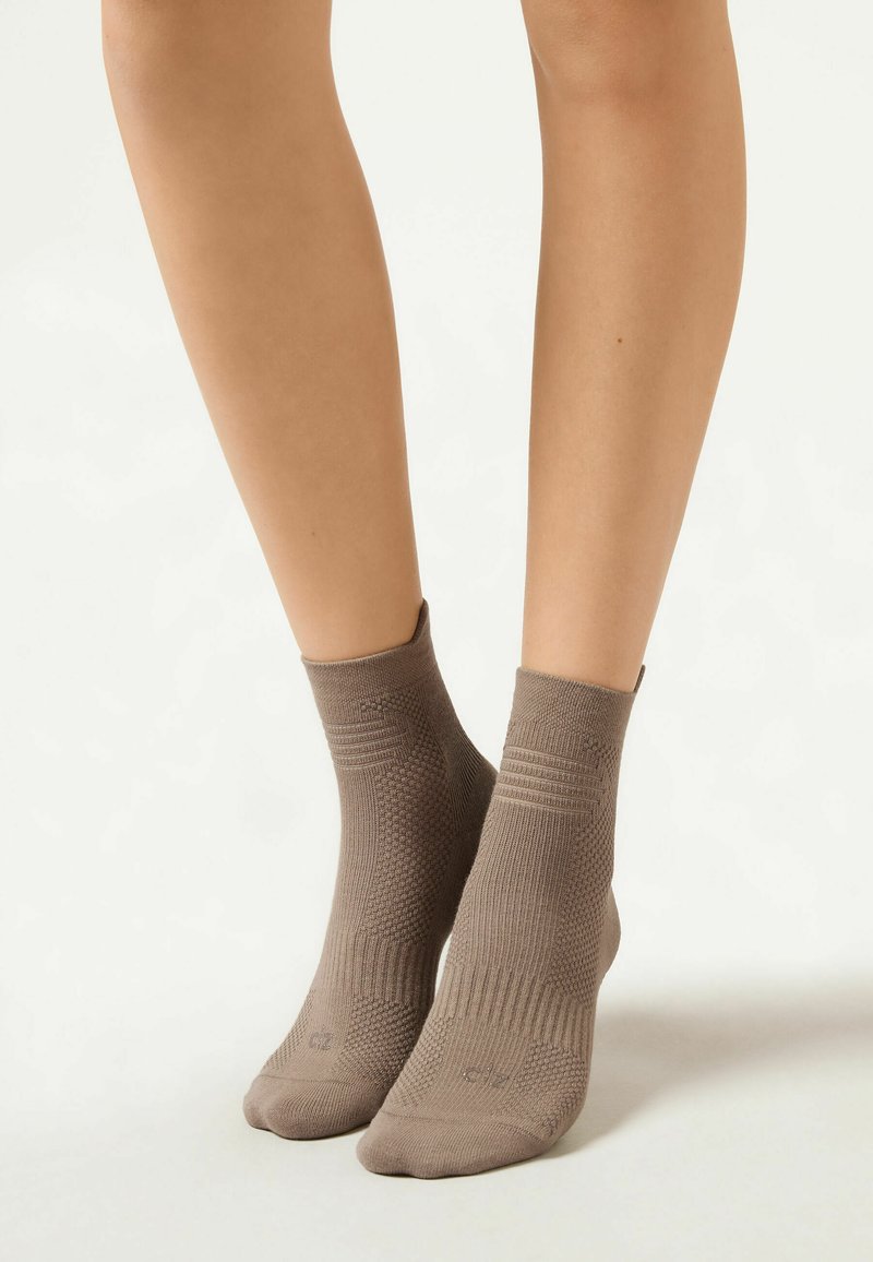 Brown knit ankle socks with a ribbed cuff and textured pattern, designed for comfort and a secure fit. Footwear covers are mid-calf length.