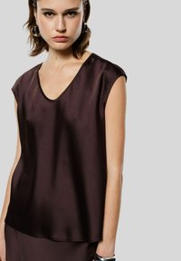 Top in satin marrone con scollatura a V e maniche a cappuccio. Texture liscia e vestibilità ampia, con dettagli di cucitura minimi.