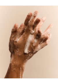 Lichtbruine handen bedekt met dikke, schuimige zeepproppen, tegen een zachte beige achtergrond samengeperst, waarbij de gladde huidtextuur wordt getoond.