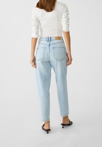 Jeans de mezclilla azul claro con cintura alta, piernas cónicas y dos bolsillos traseros. La tela parece suave con un efecto de lavado sutil.