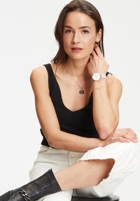 Schwarzes geripptes Tanktop, weiße verwaschene Jeans und schwarze Knöchelstiefel. Zu den Accessoires gehören eine silberne Uhr, gestapelte Halsketten und creolenohrringe.