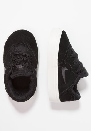 Par de zapatillas Nike negras para niños pequeños con suelas blancas, lados texturizados y cordones, mostradas desde vistas superior y lateral sobre fondo blanco.