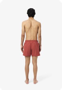 Costume da bagno rosso con vita elastica, realizzato in materiale leggero, con un design semplice e un taglio a metà coscia.