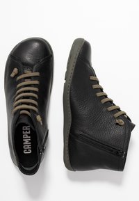 Černé kožené kotníkové boty s texturovaným povrchem, olivově zelené tkaničky, boční zip a gumová podešev. Camper logo na vnitřní stélce.