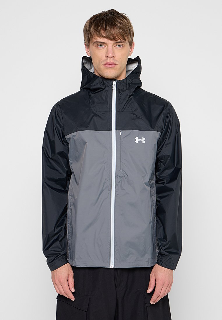 Chaqueta ligera e impermeable en negro y gris. Presenta un cierre frontal con cremallera, capucha ajustable y logo icónico en el pecho. Textura suave.