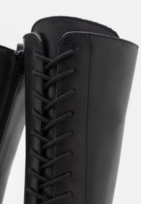 Černé kožené kotníkové boty s kulatou špičkou, hladkým povrchem, propracovaným šněrováním vpředu a bočním zipem.