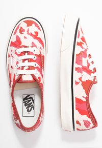 Baskets Vans avec un motif camouflage rose et rouge, tige en toile, lacets blancs et semelle en caoutchouc noire. Pr ésente des accents rouges contrastants.