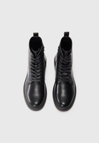 Botas negras de piel hasta el tobillo con una textura suave, presentan un cierre de cremallera y cordones planos, diseñadas con una punta redonda y un estilo minimalista.
