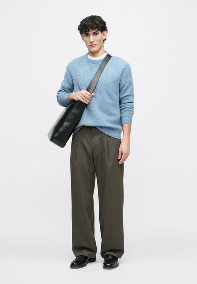 Gai zils adīti džemperis, brūni plaša kāju bikses un melna soma; modelim ir viļņaini mati, somu tur ar plecu siksnu.