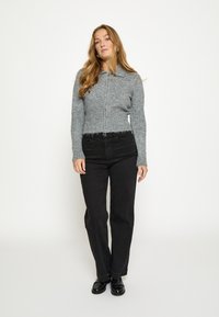 Šviesiai pilka megzta kardiganas su užtrauktuku, ribinėmis rankogaliais ir apačia. Derinama su juodomis tiesiomis kelnėmis ir juodais batais.