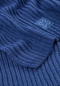 Tissu tricoté bleu avec un ribbing texturé ; présente une étiquette bleue rectangulaire avec un motif floral brodé en blanc.
