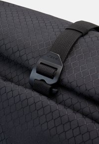 Tessuto in fibra di nylon nero con una trama a diamante, dotato di una tracolla regolabile nera e di una fibbia in plastica con il logo "Vaude" in rilievo.