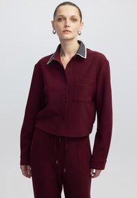 Bordeaux cropped button-down shirt met een grijze kraag, een borstzak, lange mouwen en een koordvoering onderaan. Glad, gestructureerd materiaal.