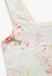 Bluse aus floraler Baumwolle in Pastellblau mit rosa und roten Blumen. Filigraner Spitzenrand entlang des Halsauschnitts und der Schulterträger.