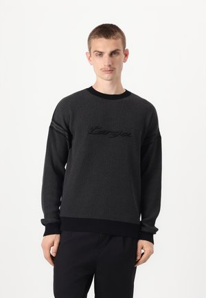 Knitted black sweater featuring a textured finish, round neckline, and ribbed cuffs. Design includes embossed logo across the chest.