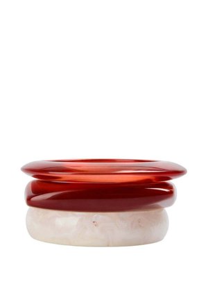 Tres pulseras lisas apiladas en resina translúcida roja y blanca marmoleada sobre un fondo blanco liso.