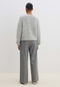 Hellgrauer, flauschiger Pullover mit gerippten Bündchen, kombiniert mit weiten grauen Hosen. Weiche Textur ist an beiden Kleidungsstücken sichtbar.