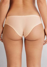 Perzikkleurige katoenen slip met een lage taille, naadloze randen en een gladde textuur, gekenmerkt door een klassieke snit en subtiele stiksel.