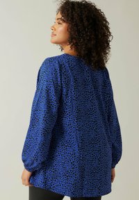 Camicia blu con motivo a macchie nere, maniche lunghe e a sbuffo, e vestibilità ampia. Tessuto morbido con una texture liscia.