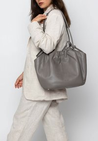 Grijze leren tote bag met een cinched top, dubbele handvatten en een gladde textuur, die een ronde vorm en kleine hardware details toont.