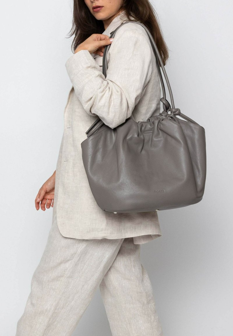 Grijze leren tote bag met een cinched top, dubbele handvatten en een gladde textuur, die een ronde vorm en kleine hardware details toont.