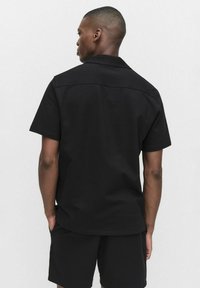 Zwarte T-shirt met korte mouwen van gestructureerde stof, met een omslaande kraag en een rechte zoom, gedragen met bijpassende zwarte shorts.