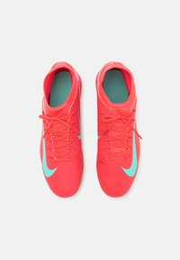 Scarpe da ginnastica rosse con tomaia testurizzata, dettagli turchesi e lacci. Presentano un design elegante e una punta arrotondata per supporto e flessibilità.