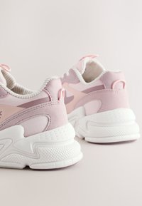 Paire de baskets roses et blanches avec des semelles épaisses texturées vues de dos sur un fond uni clair.