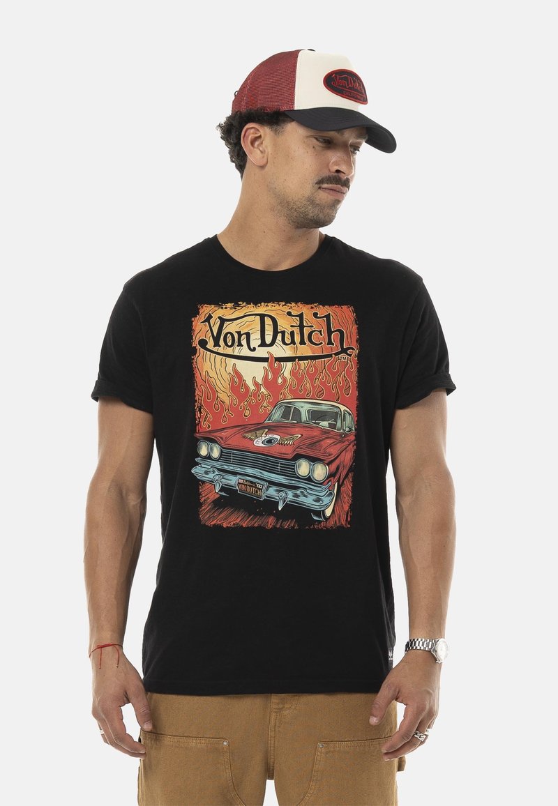 T-shirt noire ornée d'un graphique coloré d'une voiture vintage avec des flammes et le texte "Von Dutch". Le mannequin porte une casquette de baseball rouge et blanche.
