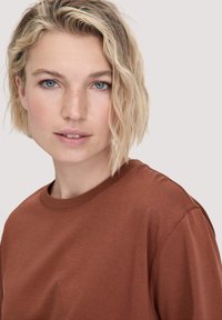 Bruine crewneck t-shirt van zacht materiaal, met korte mouwen en een ontspannen pasvorm. Gemaakt voor een model met licht, golvend haar.
