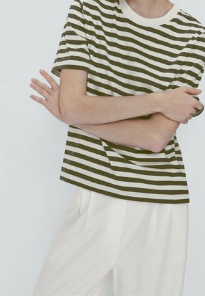 T-shirt rayé vert et blanc avec un col rond, des manches courtes et une coupe décontractée, associé à un pantalon de couleur claire.