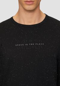 Schwarzes Langarm-T-Shirt mit gesprenkelter Textur. Mit eingeprägtem Text "SOLVER" und "SPACE IS THE PLACE" auf der Vorderseite. Runder Halsausschnitt.