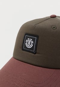 Καφέ και ελιά πράσινο καπελάκι μπέιζμπολ με μαύρο τετράγωνο ταμπελάκι που δείχνει ένα λευκό κυκλικό λογότυπο δέντρου στο μπροστινό πάνελ.