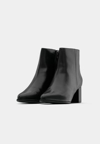 Černé kožené kotníkové boty s hladkým povrchem, špičatou špičkou a čtveratým podpatkem. Obsahují boční zip pro snadné obouvání.