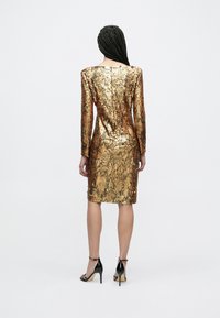 Vestido de mangas compridas, justo ao corpo, coberto de lantejoulas douradas e bronze, até ao joelho, com decote quadrado e textura lisa.