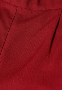 Tissu rouge profond avec un tissage serré visible et des plis cousus créant des plis subtils et une texture.
