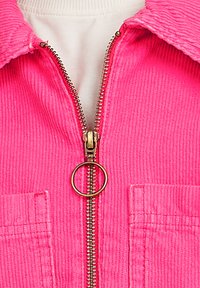 Roze corduroy jack met een gouden rits met een ronde trekker, twee voorkruizen, en een textuur van ribbelstof.