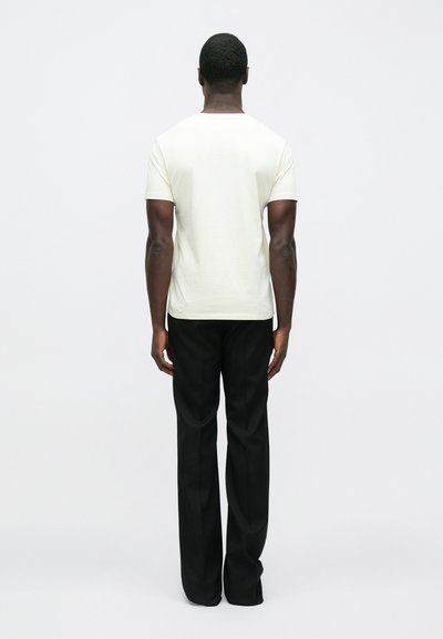Camiseta blanca de manga corta con cuello redondo, combinada con pantalones negros sueltos. Textura suave, diseño minimalista, vista desde atrás.