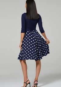 Marinblå klänning med prickar, med en figurnära bodice, trekvartsärmar och en utsvängd kjol. Tyget är slätt och lättviktigt.