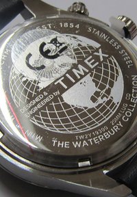 Zadnja stran jeklene ure Timex z obliko zemeljske krogle, napisom "The Waterbury Collection" in vgraviranimi podatki o modelu.