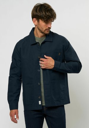 Navy blue jacket made of cotton, featuring a button closure, two front pockets, and a small logo on the chest pocket. Textured inner layer.