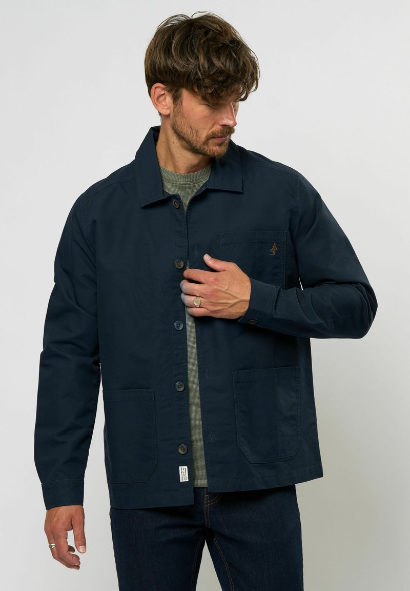 Chaqueta azul marino de algodón, con cierre de botones, dos bolsillos frontales y un pequeño logo en el bolsillo del pecho. Capa interior texturizada.